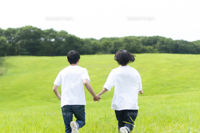 草原を走るカップルの後ろ姿 の写真素材 イラスト素材 アマナイメージズ