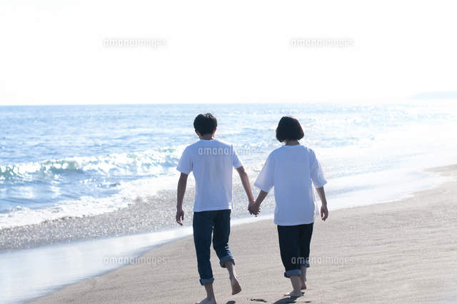 海辺を手をつないで歩くカップルの後ろ姿 の写真素材 イラスト素材 アマナイメージズ