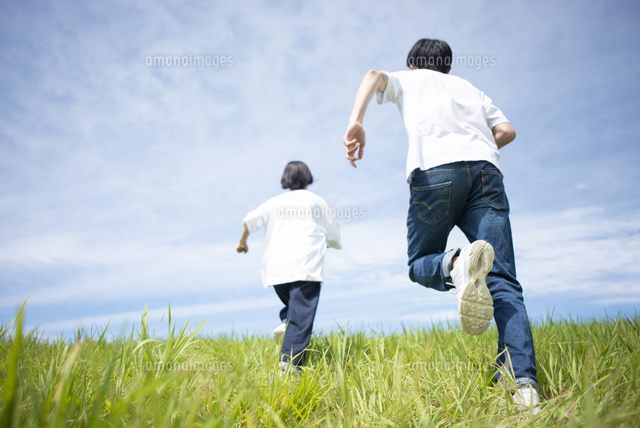 草原を走るカップルの後ろ姿 の写真素材 イラスト素材 アマナイメージズ