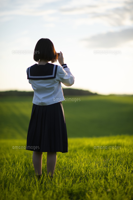 草原の中で写真を撮る女子学生の後ろ姿 の写真素材 イラスト素材 アマナイメージズ