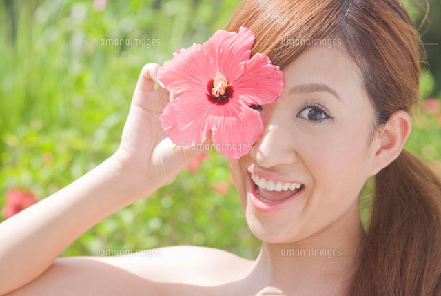 ハイビスカスの花を顔の前に持って微笑む女性[11031048298]の