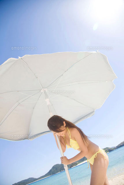 ビーチパラソルを砂浜に建てようとしている水着女性 の写真素材 イラスト素材 アマナイメージズ