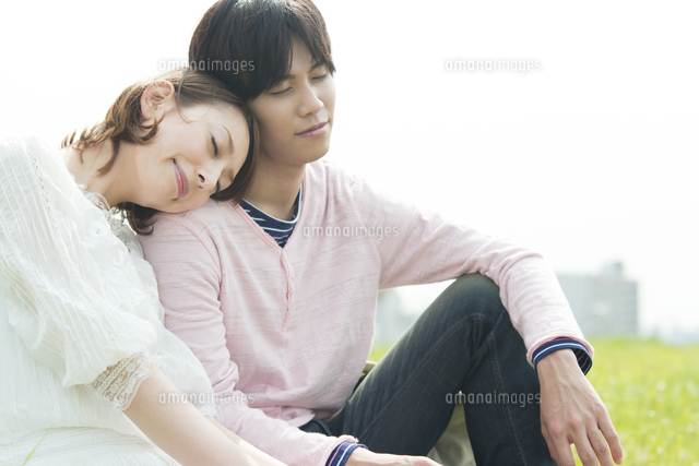 芝生に座り寄り添う男女 の写真素材 イラスト素材 アマナイメージズ
