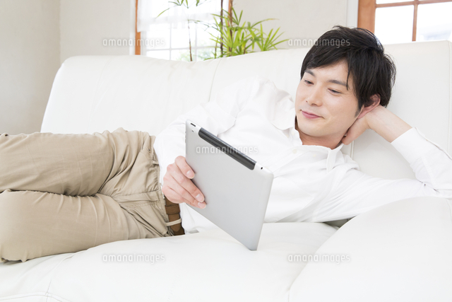 ソファーでタブレットpcを見る男性 の写真素材 イラスト素材 アマナイメージズ