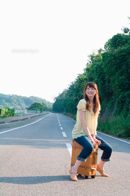 道の真ん中でキャリーケースに座る女性 の写真素材 イラスト素材 アマナイメージズ