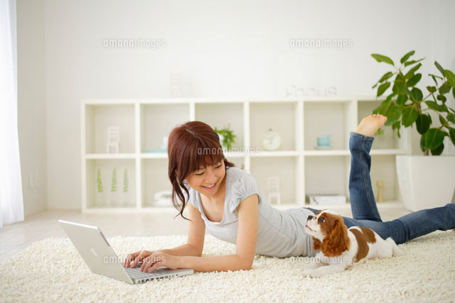 寝転んでパソコンに向う女性と犬 の写真素材 イラスト素材 アマナイメージズ