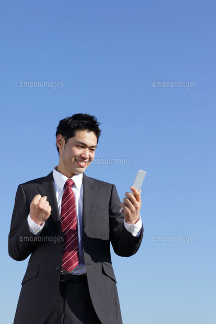 携帯を持ちガッツポーズをするスーツ姿の男性 の写真素材 イラスト素材 アマナイメージズ