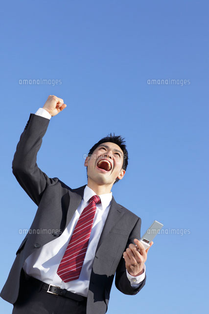 携帯を持ちガッツポーズをするスーツ姿の男性 の写真素材 イラスト素材 アマナイメージズ
