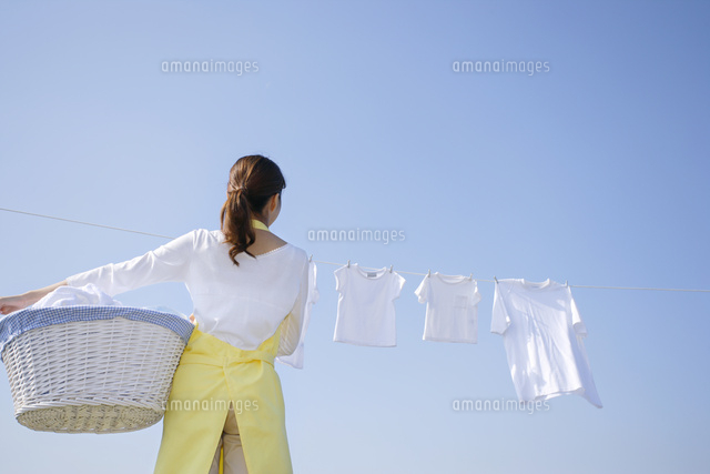 青空の下で家族の洗濯物を取り込む女性 の写真素材 イラスト素材 アマナイメージズ