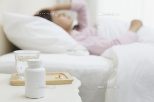 体調不良で寝る女性とテーブルに置かれた薬 の写真素材 イラスト素材 アマナイメージズ