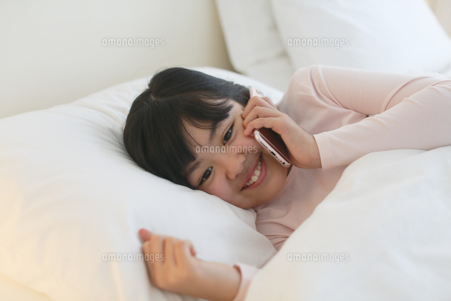 ベッドで電話をする女の子 の写真素材 イラスト素材 アマナイメージズ