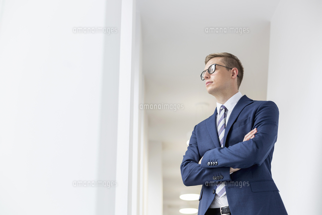 Young thoughtful businessman standing with arms crossed looking away in ...