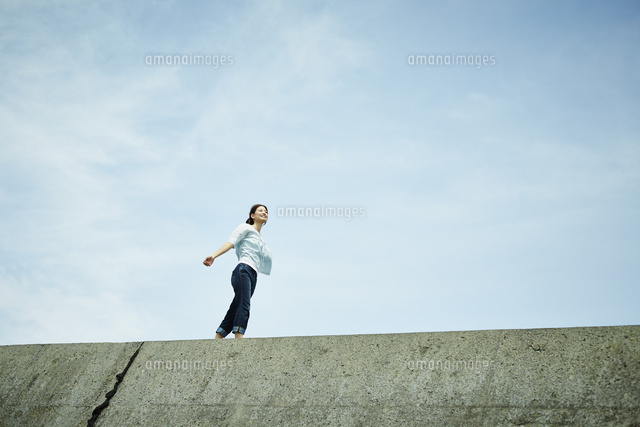 防波堤の上を歩く女性と青空 の写真素材 イラスト素材 アマナイメージズ