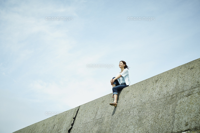 防波堤に座る女性と青空 の写真素材 イラスト素材 アマナイメージズ