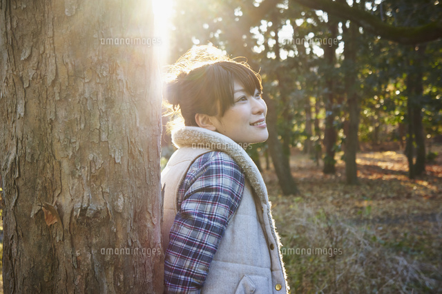 木にもたれて立つ女性と木漏れ日 の写真素材 イラスト素材 アマナイメージズ