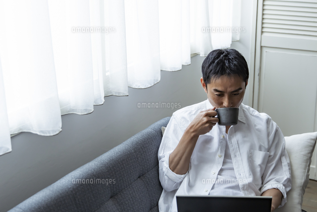 コーヒーを飲みながらノートパソコンを見る日本人男性 の写真素材 イラスト素材 アマナイメージズ