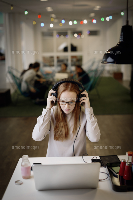Businesswoman wearing headphones while working late on laptop in ...
