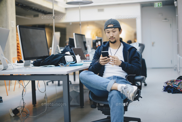 Male computer programmer using smart phone while sitting on chair in ...