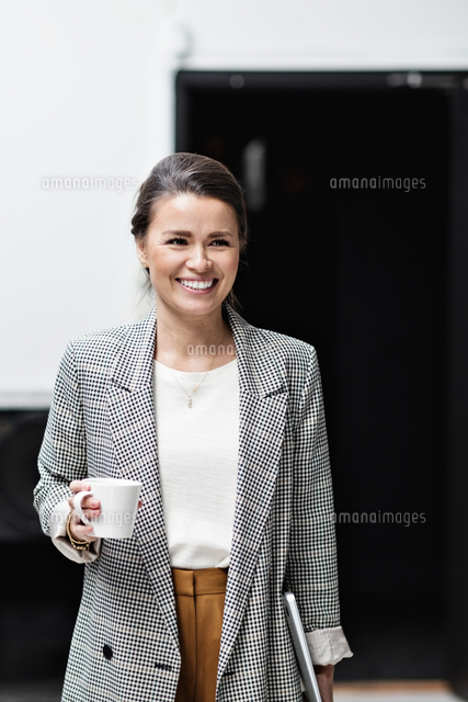 Portrait of smiling businesswoman looking away while holding coffee cup ...