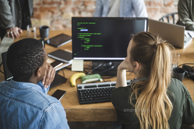 Rear view of male and female colleagues coding over computer at startup ...