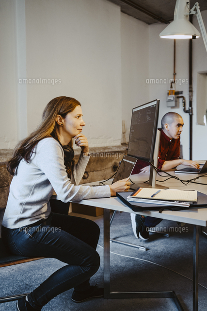 Mature female programmer coding over computer and laptop in startup ...