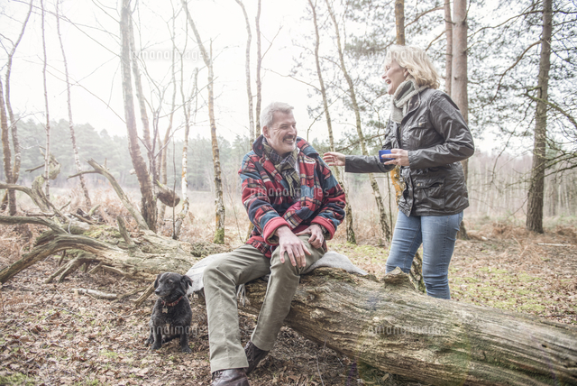 Senior couple enjoying a break with their dog during a woodland walk ...