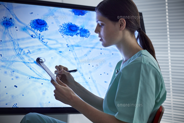 Female Nurse With Clipboard Looking At Magnified Microscope Slide On Computer Monitor の写真素材 イラスト素材 アマナイメージズ