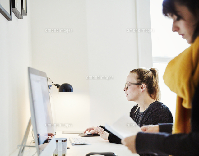 Two women in an office, one using a computer.[11093011160]の写真素材・イラスト素材 ...