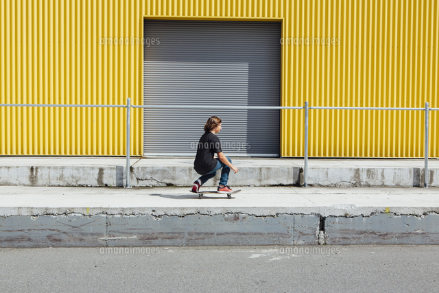 Teenage Boy Skateboarding In Front Of Industrial Warehouse Loading Zone の写真素材 イラスト素材 アマナイメージズ