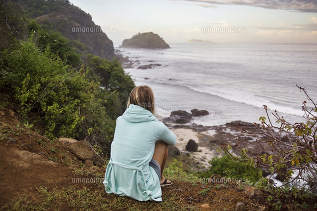 Rear view of woman looking at sea view while sitting on hill ...