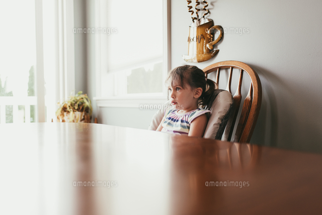 Thoughtful girl looking away while sitting on chair by wall at home ...