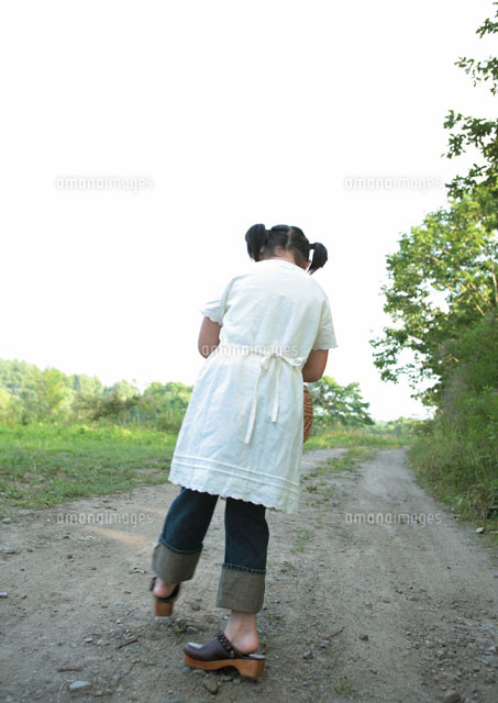 一本道を歩く女の子の後ろ姿 の写真素材 イラスト素材 アマナイメージズ