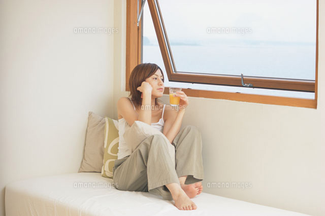 窓際のベットの上に座る女性 の写真素材 イラスト素材 アマナイメージズ