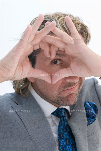 手で作ったハート型から覗く男性 の写真素材 イラスト素材 アマナイメージズ