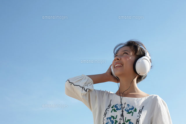 青空とヘッドフォンで音楽を聴いている女の子 の写真素材 イラスト素材 アマナイメージズ