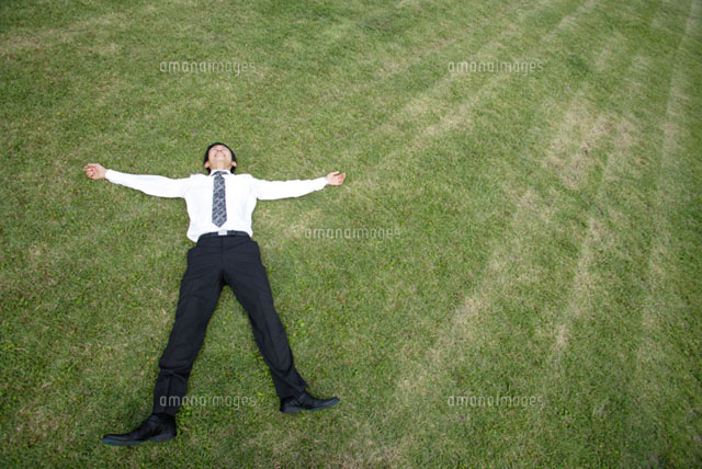 芝生の上に寝転がるビジネスマン の写真素材 イラスト素材 アマナイメージズ