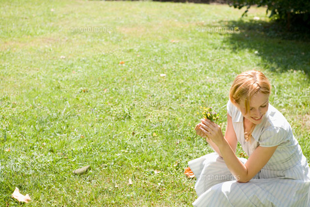芝生の上で花を持ち微笑む女性 の写真素材 イラスト素材 アマナイメージズ