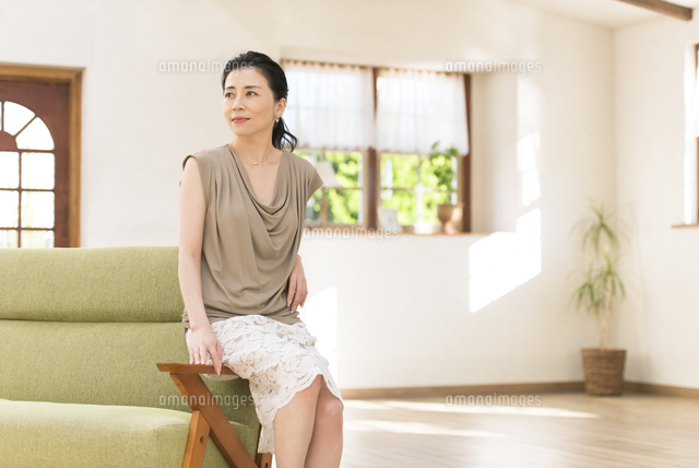 ソファーの肘掛けに腰掛ける女性 の写真素材 イラスト素材 アマナイメージズ