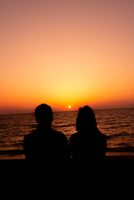 沈む夕日とカップルのシルエット[10112002933]の写真・イラスト素材