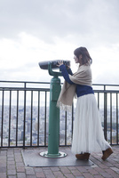 展望台から双眼鏡で神戸の景色を望む笑顔の女性[10656000156]の写真 